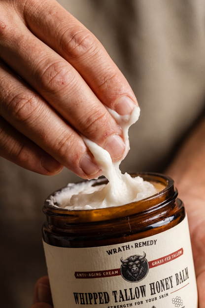 Hand squeezing whipped tallow honey balm from a jar labeled &